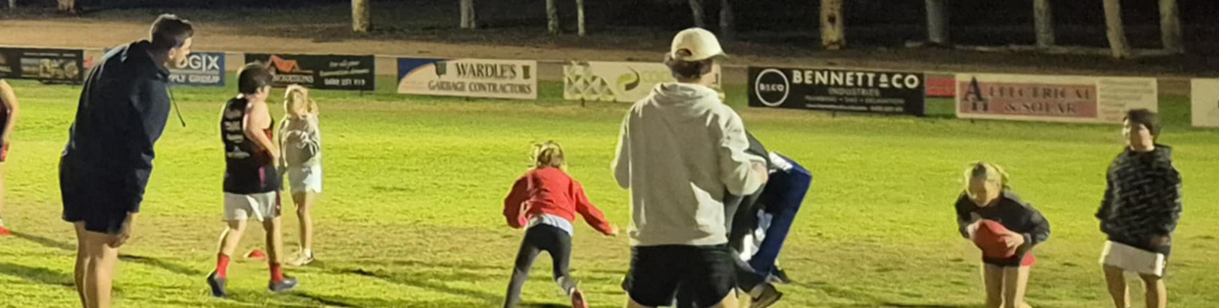 Football players and coaches running drills on oval grass
