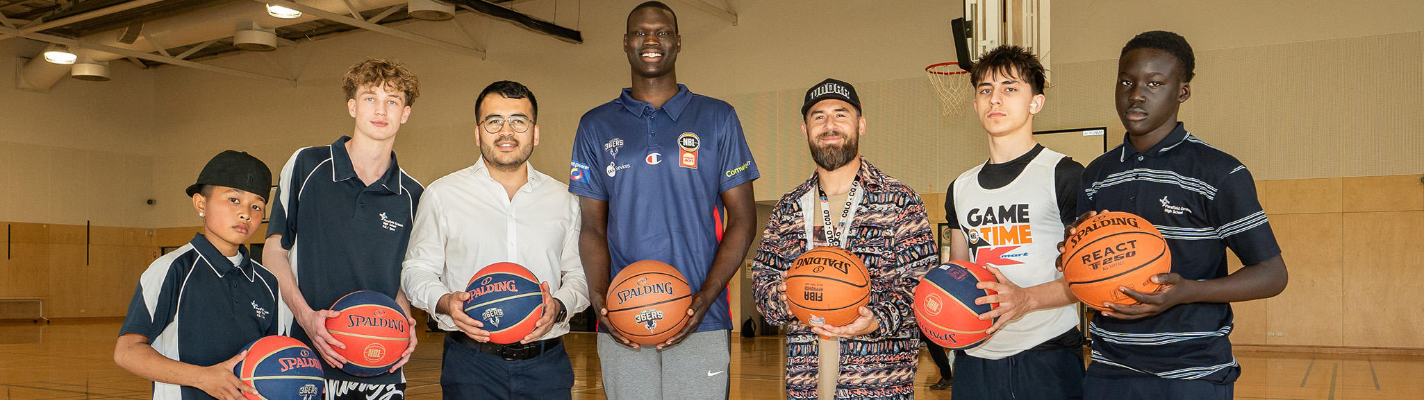Men and boys standing on a basketball court with basketballs in hand