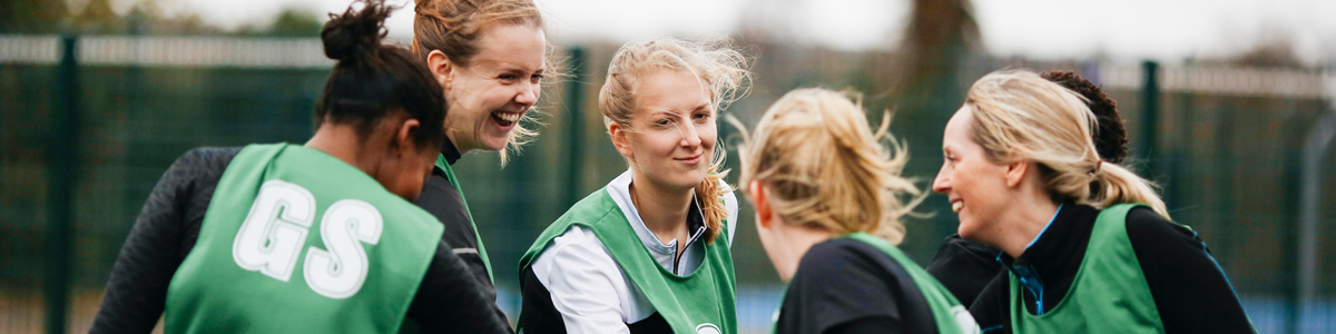 Female sports team in a group huddle wih hands in the centre
