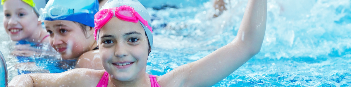 Girl in a swimming pool with a swim cap and goggles on her head