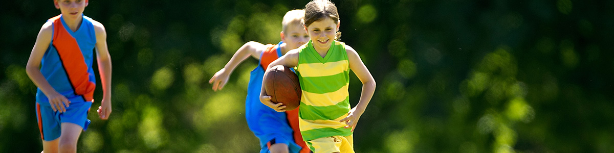 Young girl running with a football under her arm and two boys chasing her